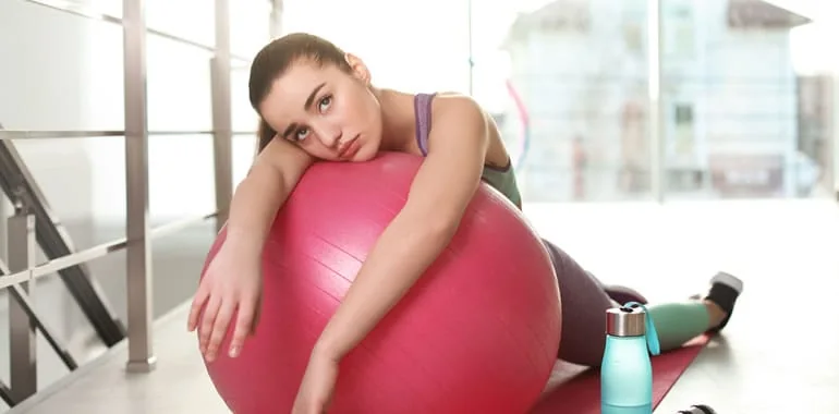 Woman resting her head on a pink exercise ball, looking exhausted after a workout
