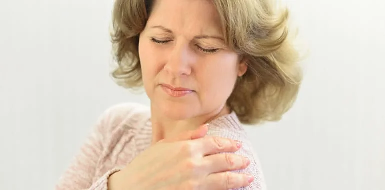 Woman with her eyes closed grimacing and holding her shoulder in pain