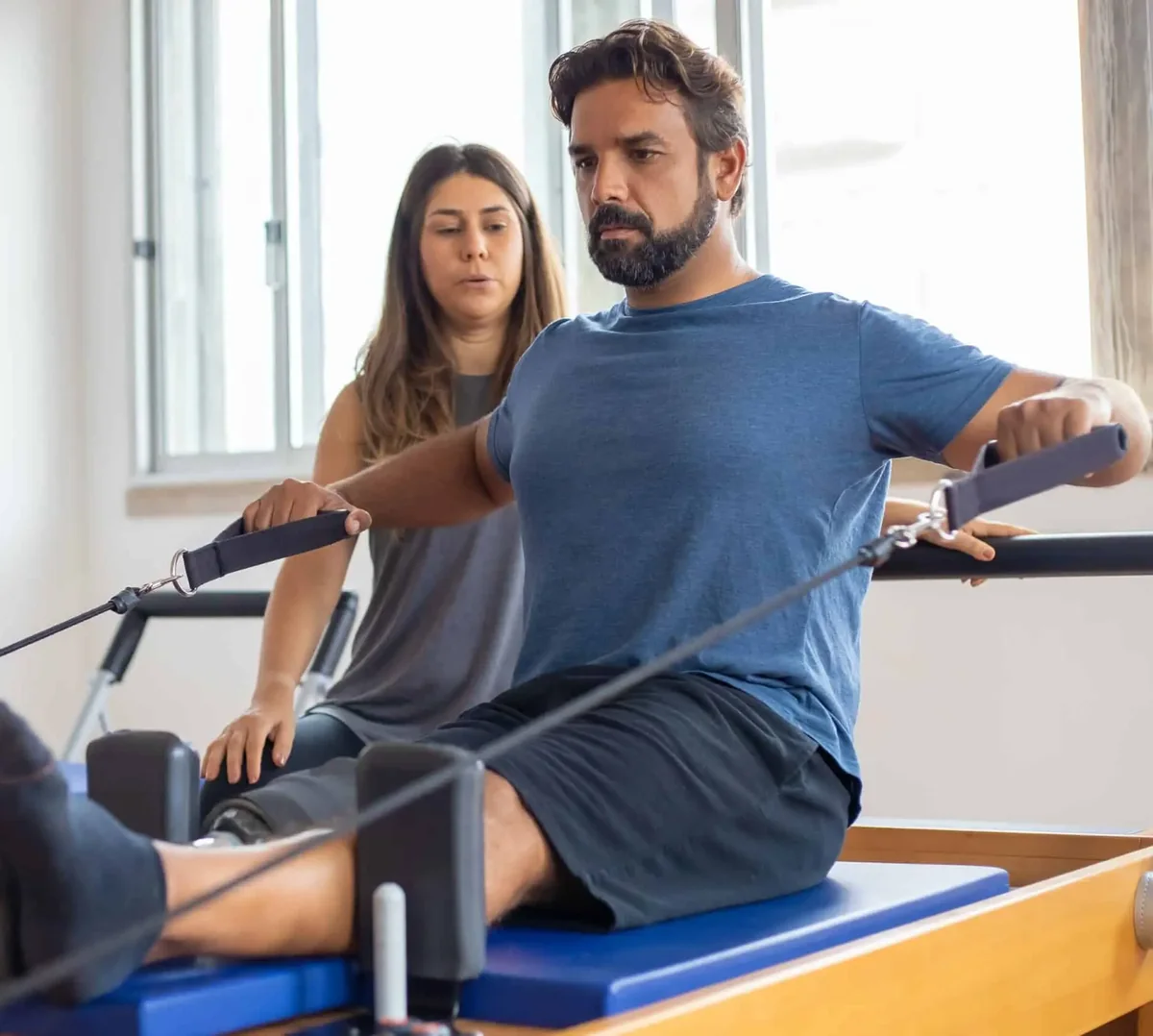 Man on a Pilates reformer pulling the straps while a woman coach watches