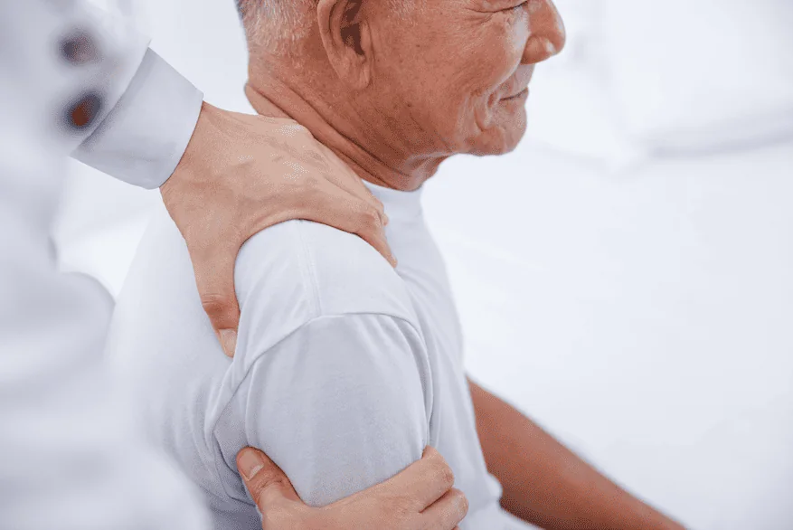 Older man receiving a therapist's hands on his shoulder and upper arm