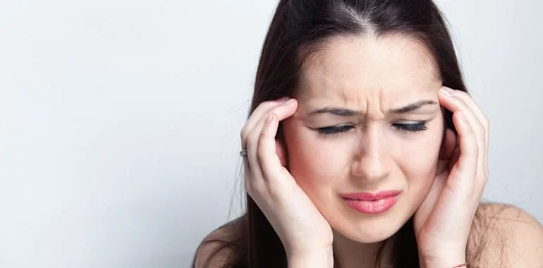 Woman wincing with her fingers pressed to her temples from a headache