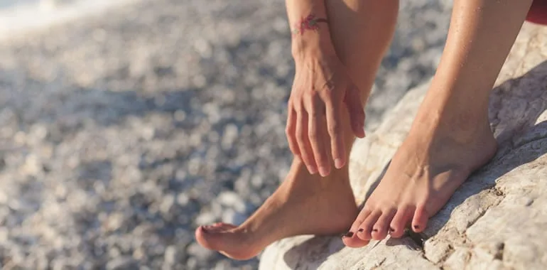 Barefoot person resting on a rock while rubbing their ankle