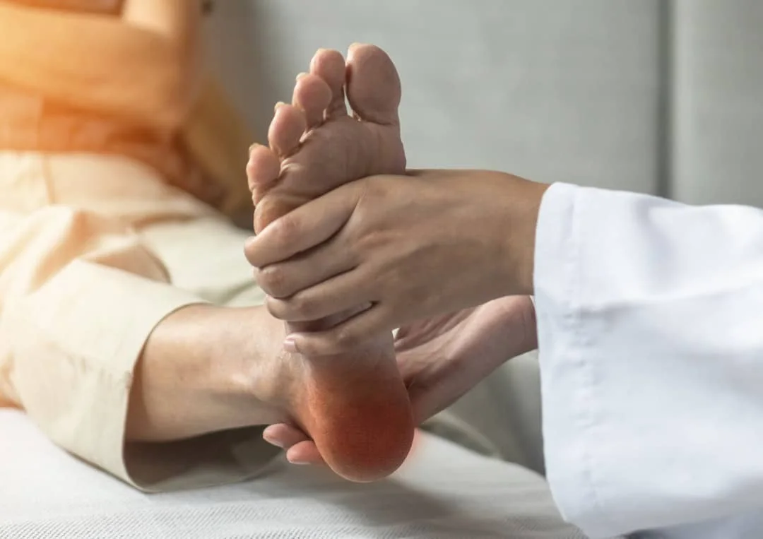 Clinician in a white coat pressing on the heel of a patient's foot, with the heel highlighted in red