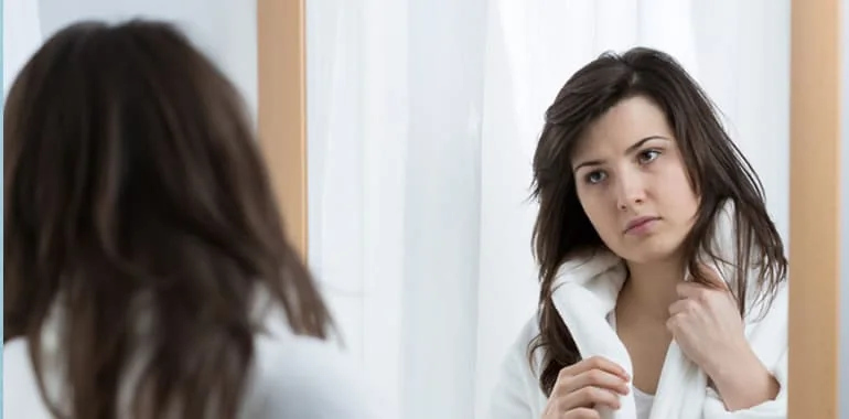 Woman in a bathrobe looking at her reflection in a mirror
