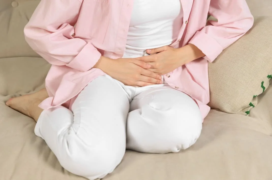 Woman seated cross-legged on a couch with her hands resting on her lower abdomen