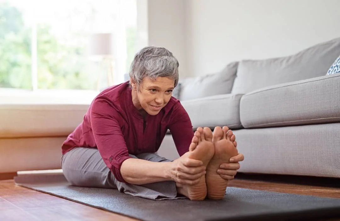 Older woman stretching forward to reach her toes on a yoga mat