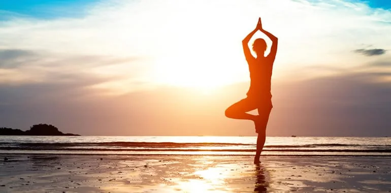 Silhouette of a person in a tree yoga pose on a beach at sunset
