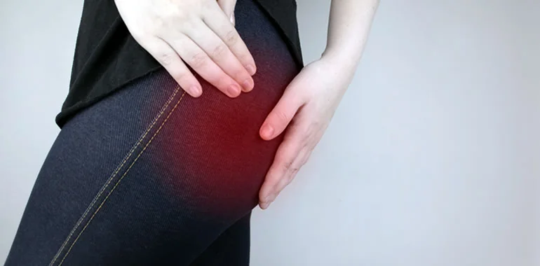 Woman holding her hip, with a red glow marking pain in the upper thigh