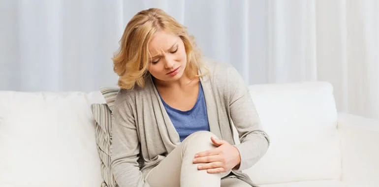 Woman sitting on a white sofa holding her knee with a pained look