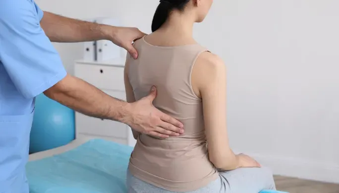 Therapist checking the spinal alignment of a seated patient for scoliosis